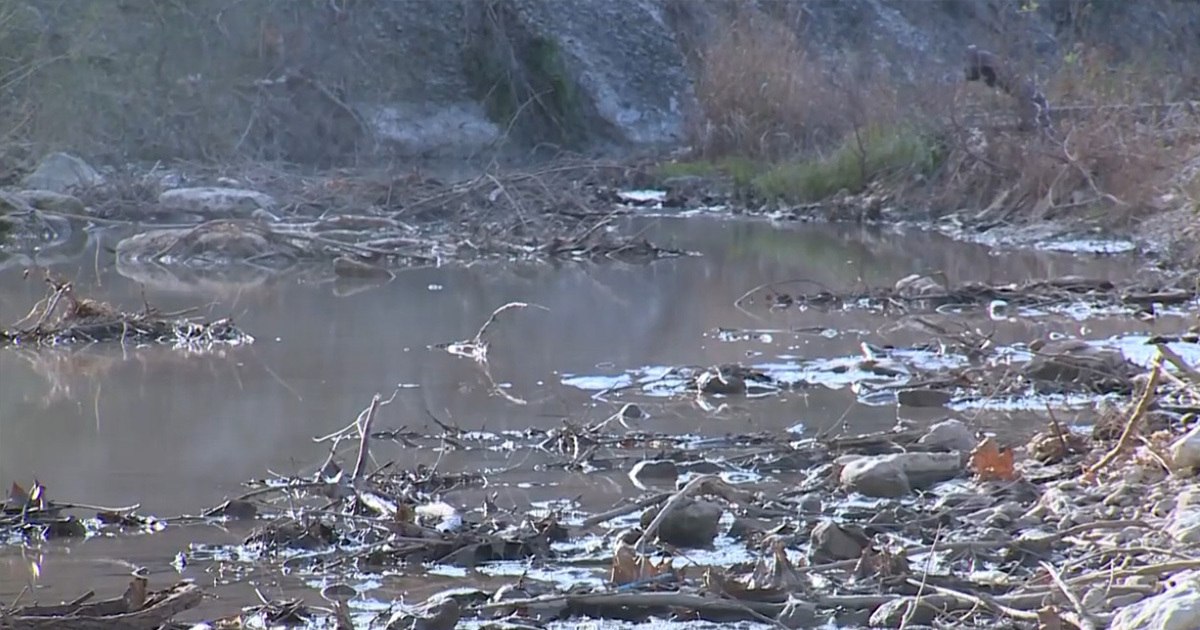 Murky water of the South Fork San Gabriel River affected by the Georgetown sewage spill near Wolf Ranch, with debris in the current.