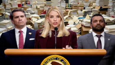 Three individuals stand behind a podium with the Department of Justice seal, addressing the press about the Epstein files. Stacks of documents fill the background, emphasizing the scale of the Jeffrey Epstein investigation. DOJ faces scrutiny over the release of Epstein files.
