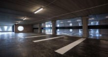 Interior of Niels Bohr car park in Lund, Sweden. Wind turbine blade curtain walls with circular cutouts provide light. Parking spaces are marked with white lines on the dark floor. This innovative Brunnshög car park showcases blade reuse.
