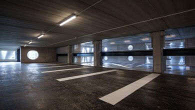 Interior of Niels Bohr car park in Lund, Sweden. Wind turbine blade curtain walls with circular cutouts provide light. Parking spaces are marked with white lines on the dark floor. This innovative Brunnshög car park showcases blade reuse.