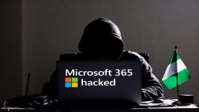 Hooded figure at a laptop with "Microsoft 365 hacked" on the screen, next to a Nigerian flag. This image relates to the recent Microsoft 365 phishing crackdown and arrest of a suspect in Nigeria.