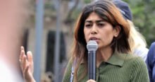 French MEP Rima Hassan speaks into a microphone, gesturing with her left hand. The pro Palestinian MEP wears a green collared shirt. Hassan barred from Canada hours before a scheduled Montreal event.