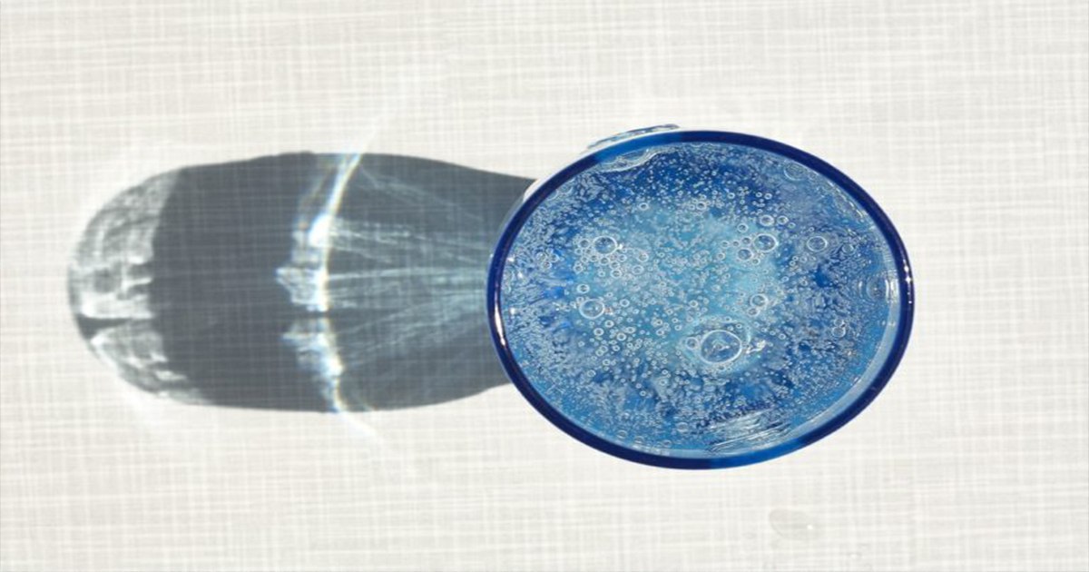 Overhead view of a blue glass filled with water and bubbles, casting a long shadow.