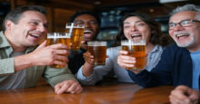 Yes, your beer tastes better ice cold, and scientists discovered why Four friends are gathered at a lively bar, each holding a glass pint of beer. Their glasses are raised in the air for a toast, and as they clink their glasses together, some beer splashes out, adding to the jovial atmosphere. They're all smiling, caught in a moment of camaraderie and celebration