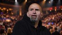Senator John Fetterman in a black hoodie on a brightly lit festival stage, evoking his Texas Tribune Festival appearance