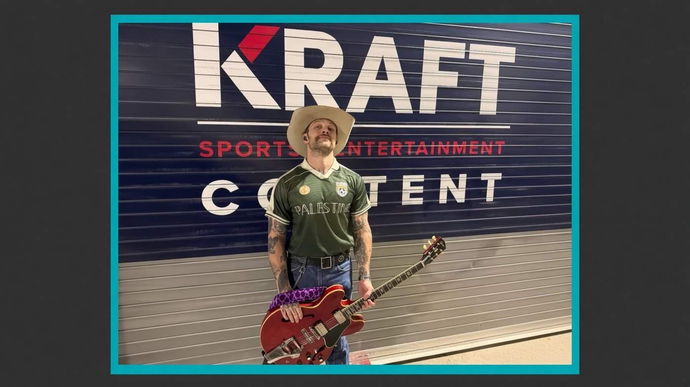 Noah Le Gros in a Palestine jersey and cowboy hat standing in front of a Kraft Sports and Entertainment sign